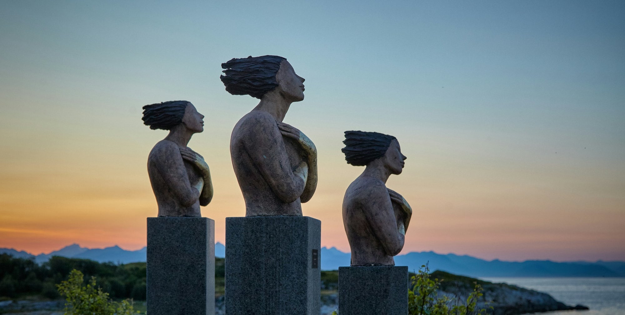 Three statues of women with hair blowing in the breeze